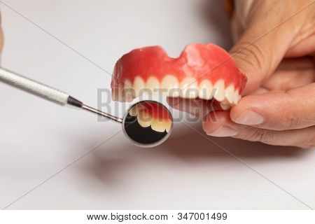 Denture prosthesis in doctor orthodentist dentist hand, checking with mirror