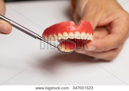 Denture prosthesis in doctor orthodentist dentist hand, checking with mirror