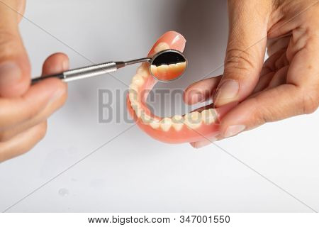 Denture prosthesis in doctor orthodentist dentist hand, checking with mirror