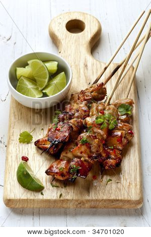 Thai chicken skewers with lime and chili, on wooden board.