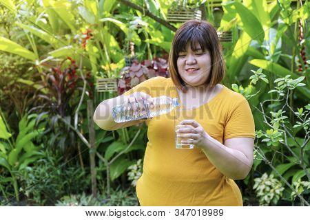 Obesity Young Woman Pouring Water From A Bottle Into A Glass While Standing In The Garden. Happiness