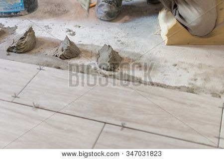 Man Installing Rectangular Shaped Floor Tiles In Kitchen. Applying Adhesive Before Installation And 