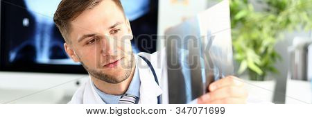 Portrait Of Concentrated Man Indicating Something On X-ray Picture With Pencil. Physician Wearing Wh
