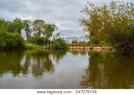 Turn The River With A Steep Bank, Overgrown With Bushes Against The Dark Low Rain Sky. Views Of The 