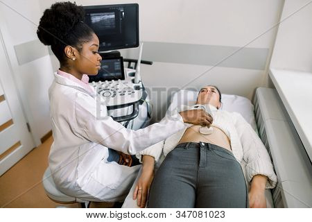 Young African Woman Doctor Moving Ultrasound Transducer On Womans Belly In Hospital. Female Doctor G