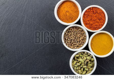Dried Colourful Spices In Small White Bowls Isolated On Black Slate Background With Space For Text