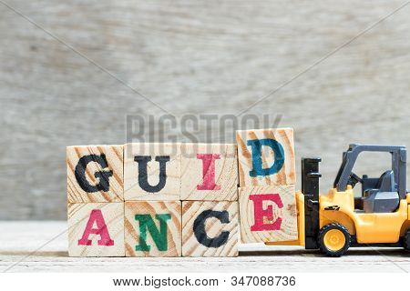 Toy Forklift Hold Letter Block D, E To Complete Word Guidance On Wood Background