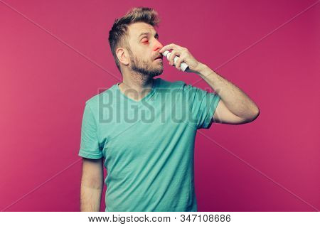 Studio Picture From A Young Man Uses Nose Spray. Sick Guy Isolated Has Runny Nose. Man Makes A Cure 