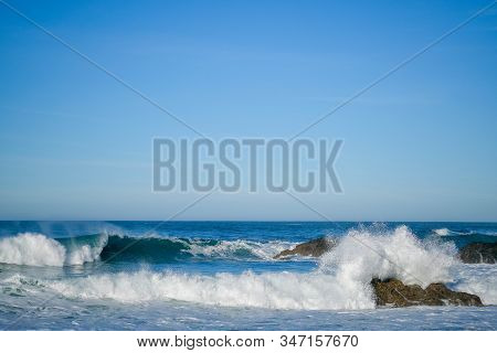 Large Ocean Waves Crash Against Coastal Stones On A Clear Sunny Day On The European Coast. Winter Ho