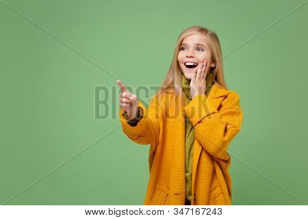 Excited Little Blonde Kid Girl 12-13 Years Old In Yellow Coat Posing Isolated On Pastel Green Backgr