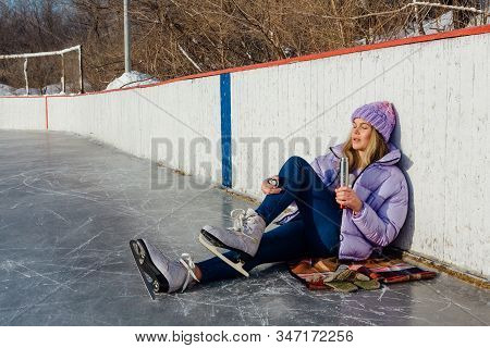 Lovely Young Woman Relaxing After Riding Ice Skates And Drinking Hot Drink From Termo Pot On The Ice