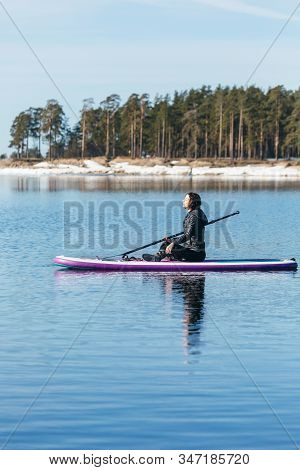 Calm Beauty Woman Sit On The Sup Board In The Middle Of Lake. She Holds Oar In Her Hand. Female On S