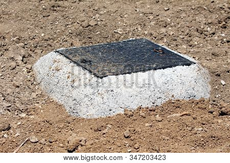 Dirt Covered New Dark Heavy Metal Rectangular Manhole Cover Surrounded With Concrete Foundation And 