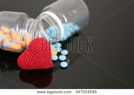 Pills And Knitted Red Heart On Dark Glass Table, Bottle With Medication In Capsules. Concept Of Hype