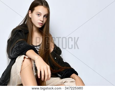 Brunette Teenager With Long Hair, In Striped T-shirt, Black Denim Jacket, Beige Pants And Sneakers. 