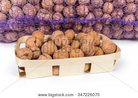 Ripe Whole Walnuts In Samall Wooden Basket Against The Nuts In Large Plastic Mesh Bag On A White Bac