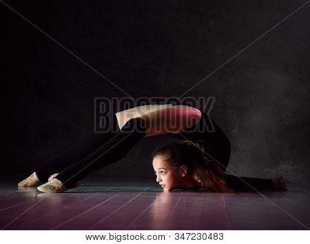 Young Girl Gymnast In Black Sport Body And Uppers Lying On Floor On Neck With Streched Back And Body
