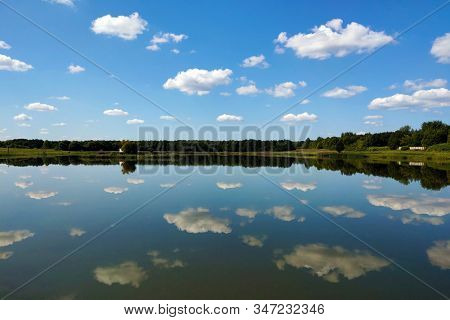 Reflection Of The Sky In Water, A Beautiful Background With Blurry Reflection Of Green Trees And Whi