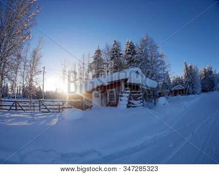 Red Lapland Wooden Hut In The Winter Snow With Sunburst