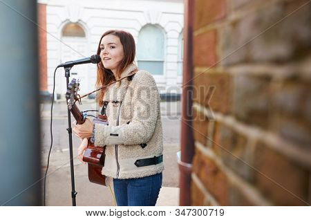Female Musician Busking Playing Acoustic Guitar And Singing Outdoors In Street