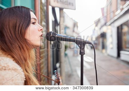 Female Musician Busking Playing Acoustic Guitar And Singing Outdoors In Street