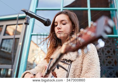 Female Musician Busking Playing Acoustic Guitar And Singing Outdoors In Street