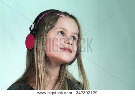 Pretty Smiling Cild Girl Listening To Music In Big Pink Earphones.