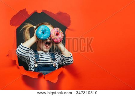 Happy cute boy is having fun played with donuts on Lush Lava background wall. Bright photo of a boy. Colored donuts