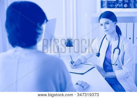 Doctor and patient discussing medical problems in a hospital consulting room. Doc filling in a patient's form