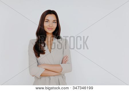 Studio Shot Of Attractive Woman Stand With Crossed Hands, Wears Formal Clothing, Has Dark Long Hair,