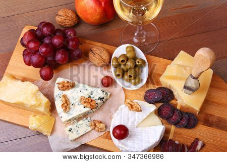 Assortment Of Cheese With Fruits, Grapes, Nuts, Glass With Wine And Cheese Knife On A Wooden Serving