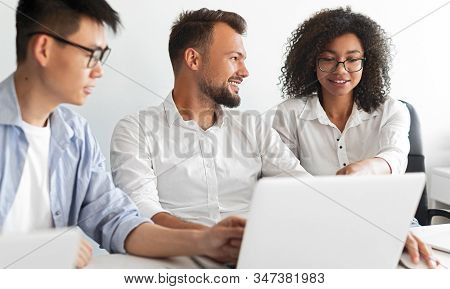 Optimistic Diverse Men Smiling And Listening To Black Woman While Browsing Laptop And Working On Pro