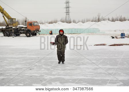 An Installer In Green Winter Workwear Walks Along An Assembly Site Against A Background Of Stacked B