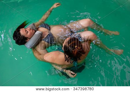 High Angle View Of Female Professional Therapist Helping Relaxed Pregnant Woman In Swimming Costume 
