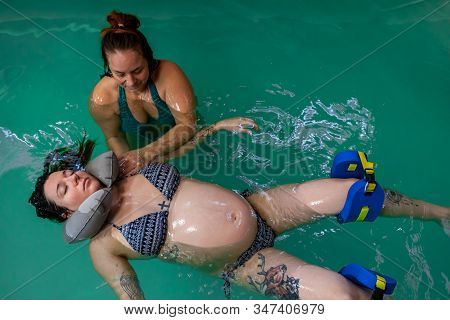 High Angle View Of Female Therapist Helping Relaxed Pregnant Woman. With Neck And Lef Float To Float