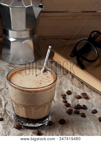 Fresh Coffee In A Glass With Cream And Coffee Beans On A Paper Background. Near Moka Pot And Book. C