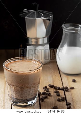 Coffee In A Glass With Cream And Coffee Beans On A Wooden Background. Near Moka Pot And Milk Jug. Cl