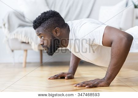 Young Black Man Exercising In His House Gym, Doing Push Ups, Side View, Free Space