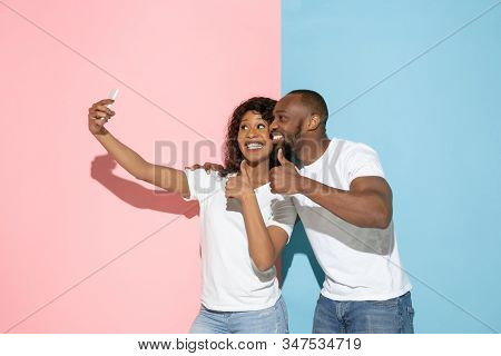 Taking Selfie. Young Emotional Man And Woman In Casual Clothes On Pink And Blue Bicolored Background