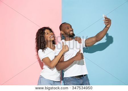 Taking Selfie. Young Emotional Man And Woman In Casual Clothes On Pink And Blue Bicolored Background