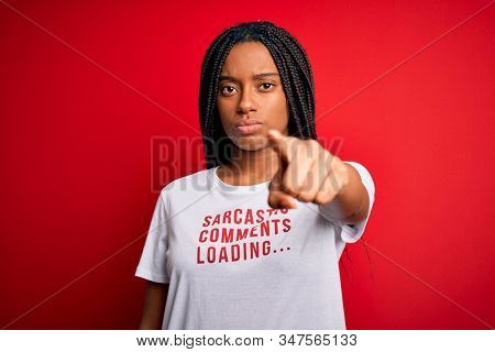 Young african american woman wearing sarcasm coments text on t-shirt over red background pointing with finger to the camera and to you, hand sign, positive and confident gesture from the front