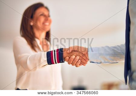Two middle age business workers smiling happy and confident. Working together with smile on face doing handsake at the office