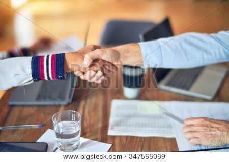 Two middle age business workers smiling happy and confident. Working together with smile on face using laptop doing handsake at the office