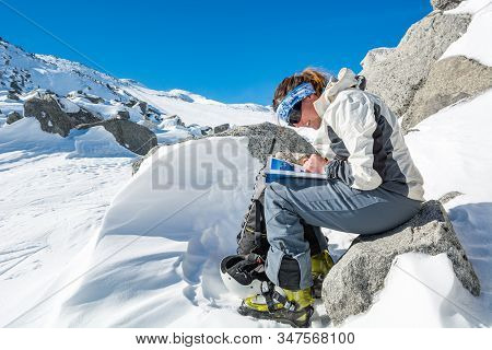 Female Mountaineer Reading A Guide Book In The Mountains To Find A Way.
