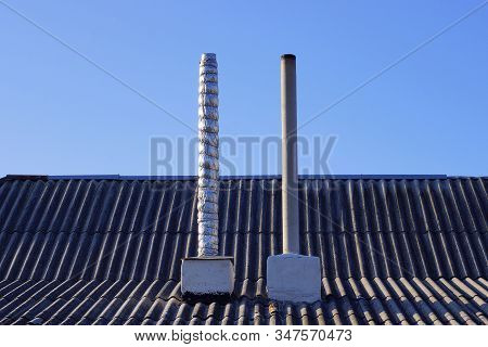 Two Long Gray Chimney Pipes On A Slate Roof Against A Blue Sky On A Sunny Day