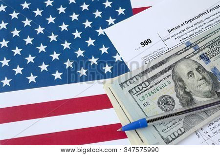 Form 990 Return Of Organization Exempt From Income Tax And Blue Pen With Dollar Bills Lies On United