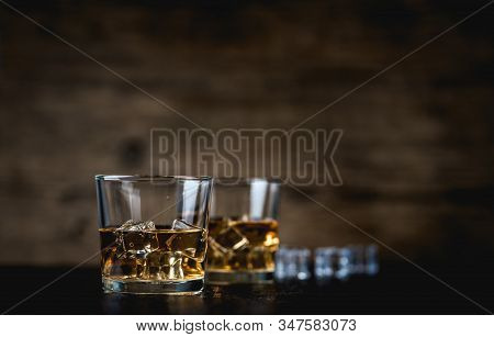 Whisky, Whiskey, Bourbon Or Cognac With Ice Cudes On Black Stone Table And Wood Background