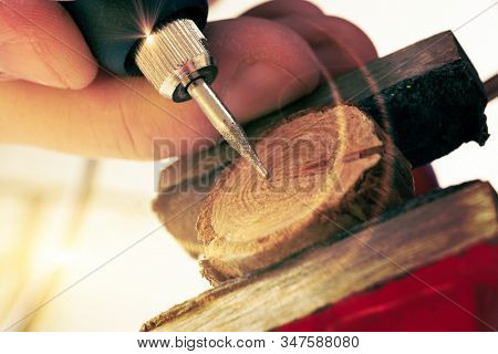 Woman using a high speed rotary multi tool to engrave ornament on slice of wood. Tool could be used as grinder
