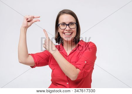 Pretty Amazed Woman In Red Shirt And Glasses Shows Something Invisible With Her Fingers.