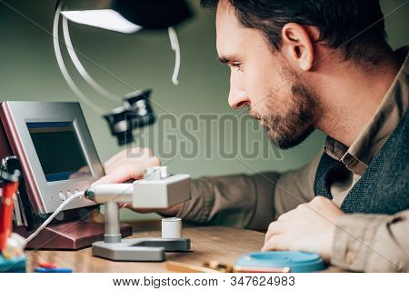Side View Of Watchmaker Using Timegrapher While Working At Table